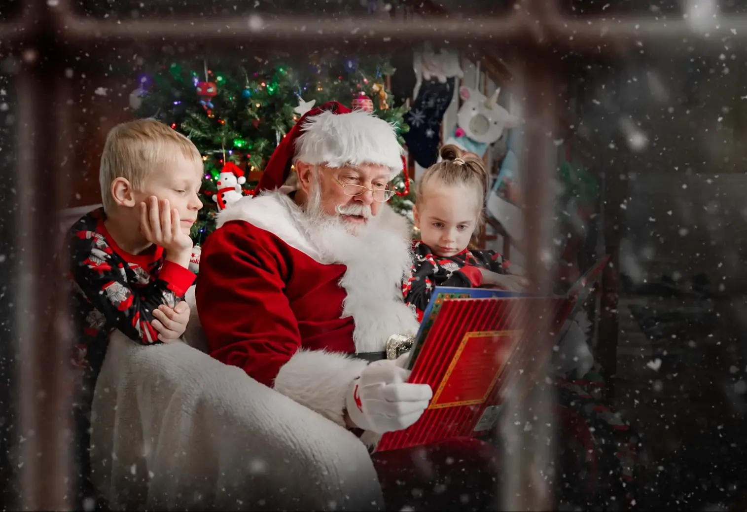 Santa Skip reading with two children beside a Christmas tree